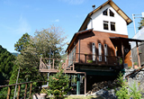 緑豊かな自然の中に建つ木造デッキがついた住居の外観の写真