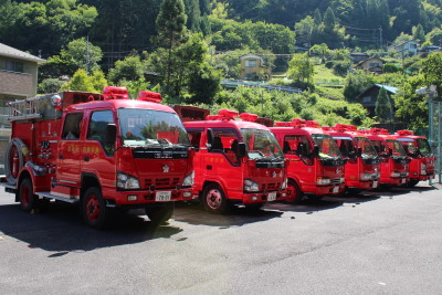 赤い消防団車両が6台並んで停めてある写真
